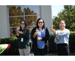 Three women outside holding ice cream and smiling standing in front of shrubs and a building.