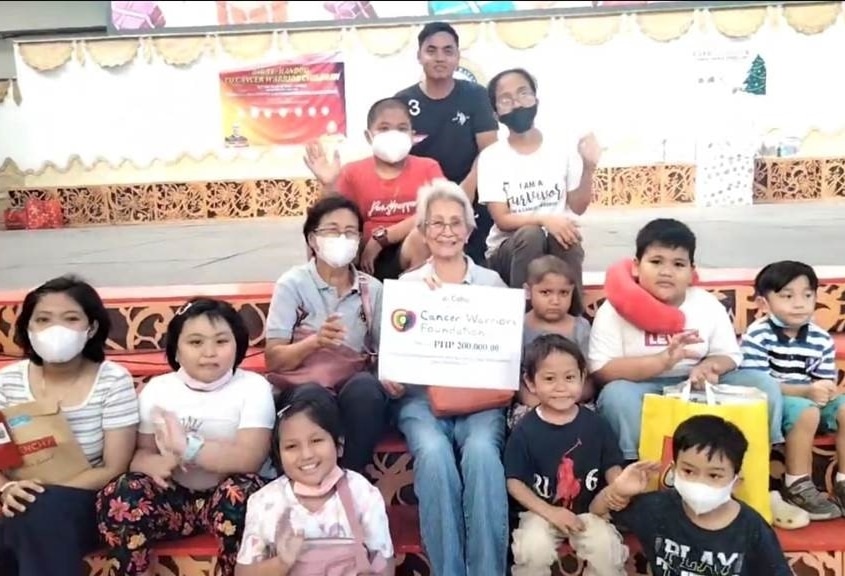 A group of 13 people smiling and sitting on steps. At least eight are children and are waving.