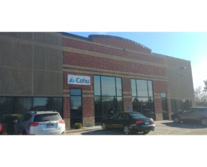 A brick building with tall windows and three cars parked out front.