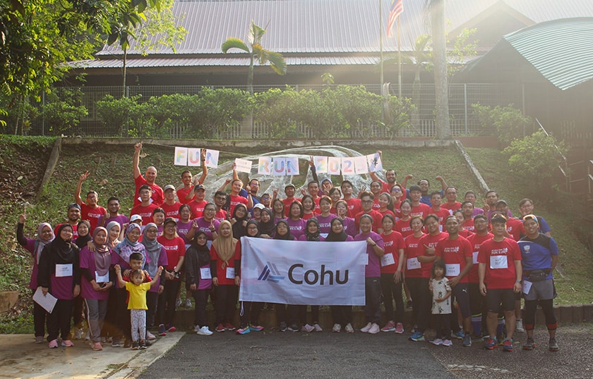 Approximately 70 people smiling in a group outside holding a banner that reads Cohu and individual letters that spell out Fun Run 2024.