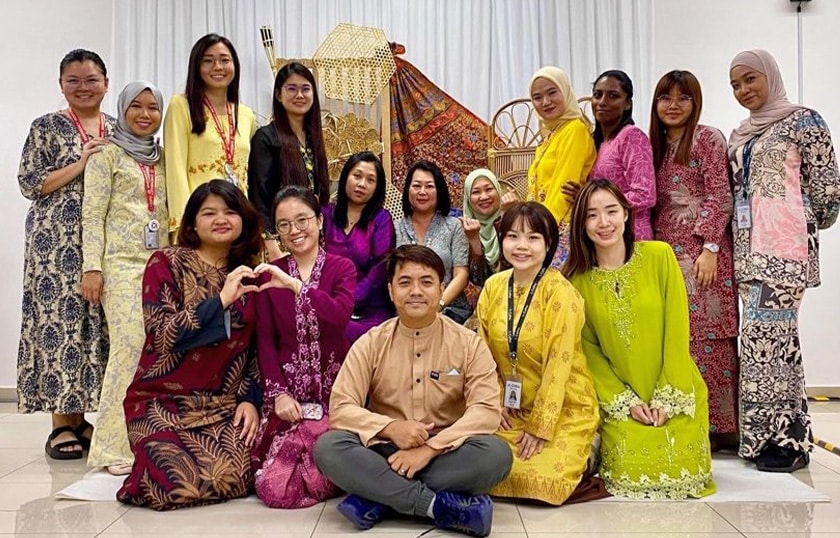 A group of 16 people wearing colorful outfits in celebration of Eid al-Fitr in an office setting.