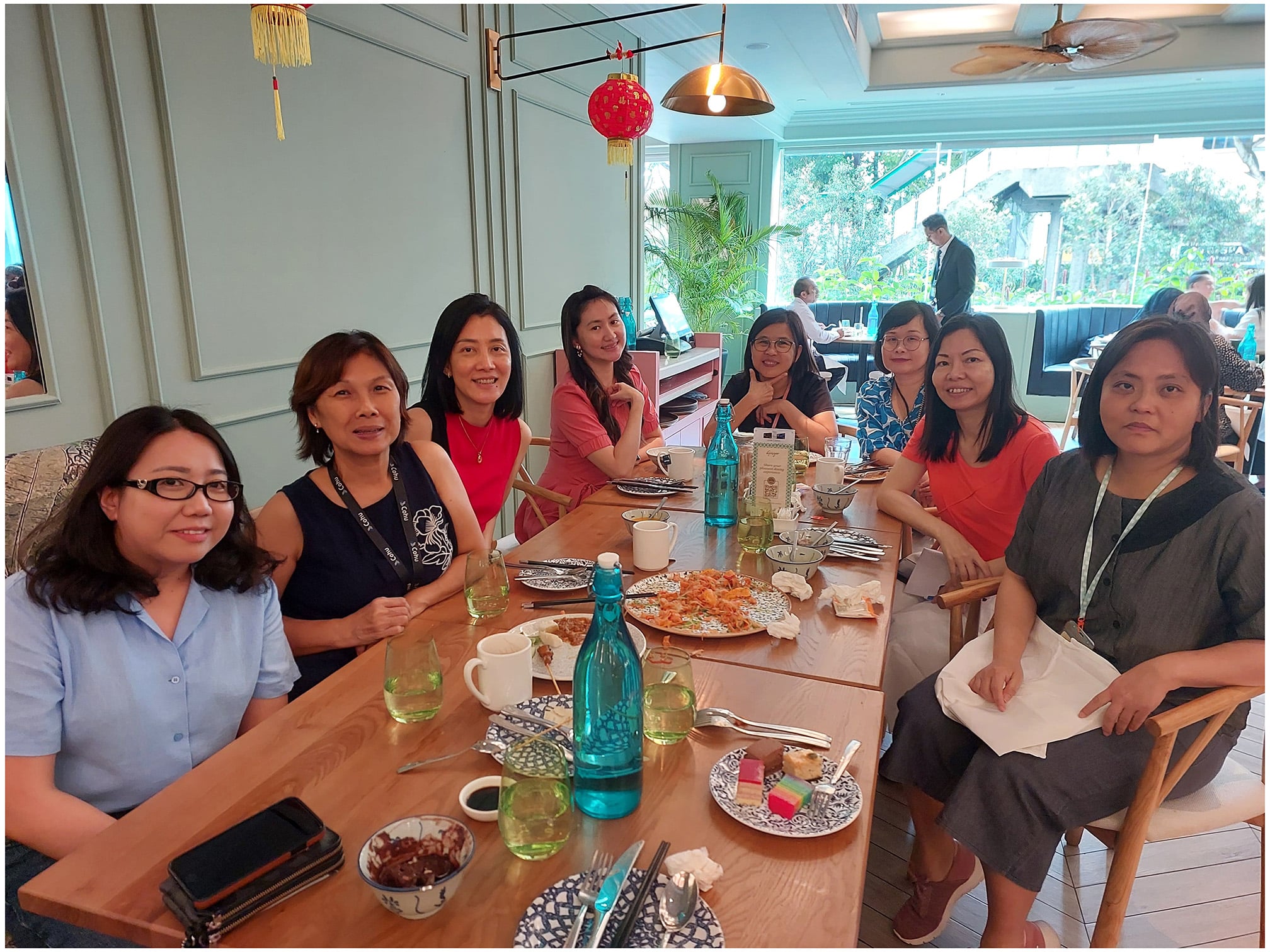 Eight women sitting at a table at a restaurant smiling with half eaten plates of food and drinks on the table.